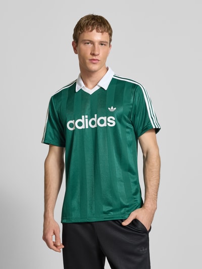 Männermodel trägt Trikot mit Umlegekragen und Label-Print von adidas Originals, Herren, Regular Fit, V-Ausschnitt, Ganzkörperansicht von vorne.