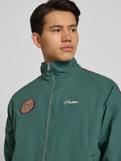 Männermodel trägt Trackjacket mit Label-Stitching Modell 'Slipstream' von PROHIBITED in Grün, Reißverschluss, Stehkragen, Nahaufnahme Oberkörper.