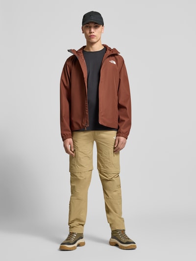 Männermodel trägt Jacke mit Kapuze von The North Face in Braun, Regular-Fit, mit Label-Print und Reißverschlusstaschen, Ganzkörperansicht von vorne. Rückenlänge bei Größe L: 76 cm, Schulterbreite: 48 cm, Brustweite: 68 cm, Ärmellänge: 68 cm.