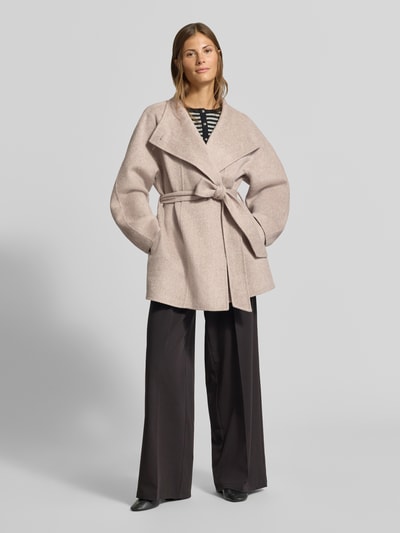 Frauenmodel trägt Mantel mit Woll-Anteil von MYON in Beige, lockerer Schnitt, Stehkragen, Taillenband, Ganzkörperansicht von vorne.