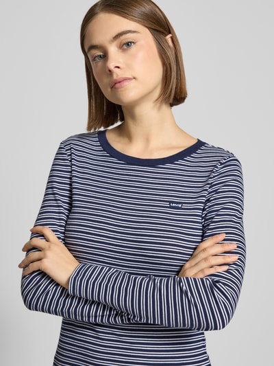 Modelka kobieca nosi Slim Fit Longsleeve mit Logo-Stitching Modell 'Essential' od Levi's®, bawełna, granatowo-białe paski, ujęcie z przodu, zbliżenie na górną część ciała.