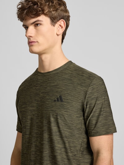 Männermodel trägt T-Shirt mit Label-Print von adidas Training in Olivgrün, Material-Mix mit Stretch, Nahaufnahme Oberkörper.