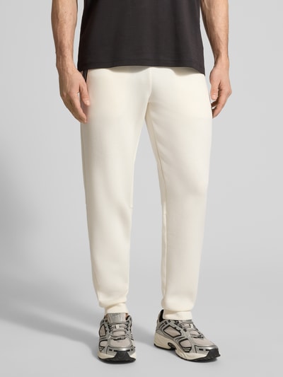 Männermodel trägt Sweatpants mit Viskose-Anteil Modell 'TRAIN PREMIUM SHIELD' von EA7 Emporio Armani, cremefarben, Nahaufnahme Oberkörper bis Füße, gerade Passform, elastischer Bund, Reißverschlusstaschen, gerippte Abschlüsse, Material-Mix.