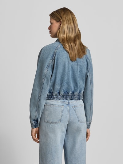 Frauenmodel trägt Relaxed Fit Jeans-Bomberjacke aus Baumwoll-Mix von Hugo Blue in Denim-Optik, helle Blautöne, strukturierte Oberfläche, Ganzkörperansicht Rückansicht.