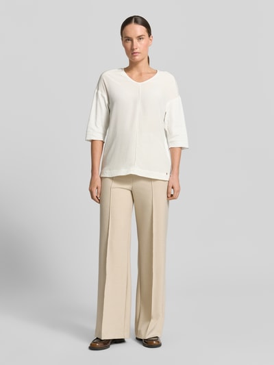 Frauenmodel trägt T-Shirt mit Ärmelaufschlag und Rundhalsausschnitt von Marc Cain aus Baumwoll-Mix mit Stretch-Anteil, Straight Fit, Label-Detail, Rückenlänge bei Größe 36: 62 cm, cremefarbene Textur, Ganzkörperansicht von vorne.
