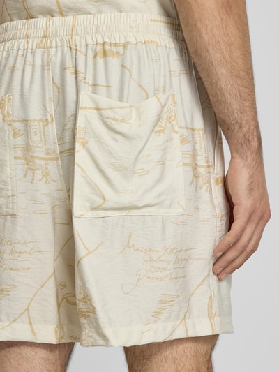 Männermodel trägt Shorts aus Viskose-Mix von MAISON KITSUNÉ in Hellbeige mit Crinkle-Optik, elastischem Bund und Eingrifftaschen, Detailaufnahme von schräg hinten.
