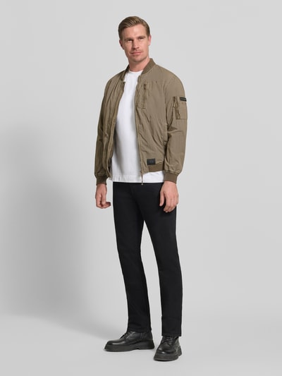 Männermodel trägt khakifarbenen Blouson mit Label-Patches Modell 'IBE' von khujo, Gerader-Schnitt, Stehkragen, Ganzkörperansicht von vorne.