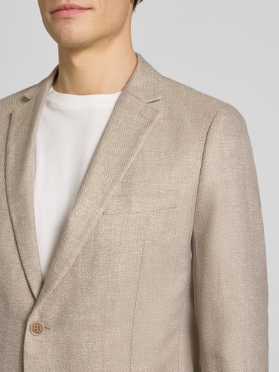Męski model nosi Regular Fit Anzugsakko aus Leinen-Mix von s.Oliver BLACK LABEL, melange, krój regular fit, tkanina o grubej teksturze, detal: dwurzędowe rozcięcie, kieszenie z klapkami, revers, lniany materiał, jasny beż, zbliżenie górnej części ciała