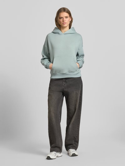 Frauenmodel trägt Hoodie mit Logo und Känguru-Tasche von Review aus Baumwoll-Mix, Relaxed-Fit, hellblau, vorne, Ganzkörperansicht von vorne.