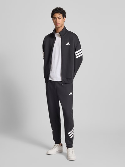 Mannelijk model draagt Sweatpants met elastische tailleband van adidas Sportswear, katoenmix, losse fit, labelprint, zwart-wit, volledige lichaamsvoorzijde.
