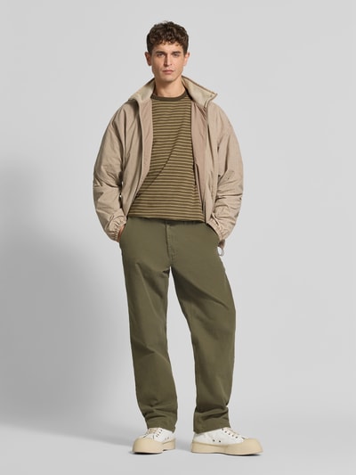 Männermodel trägt Relaxed Fit T-Shirt mit Label-Stitching von Forét, reine Baumwolle, Rundhalsausschnitt, Halbarm, Olivgrün, Ganzkörperansicht von vorne.