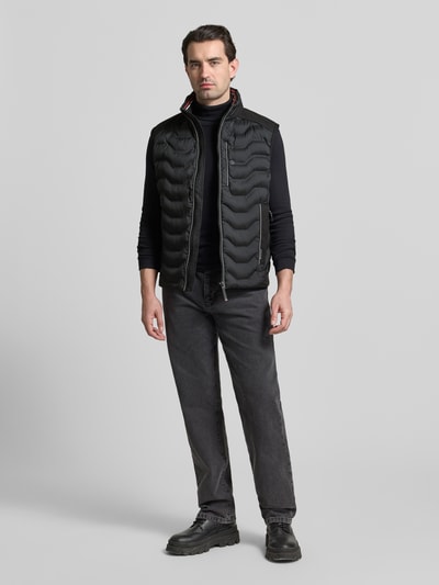 Männermodel trägt Regular Fit Steppweste mit Kapuze im Kragen von Tom Tailor in Schwarz, Reißverschluss, Label Patch, Ganzkörperansicht von vorne.