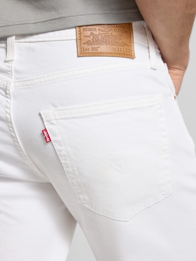 Mężczyzna nosi Tapered Fit Jeans aus Baumwoll-Lyocell-Mix Modell '502™ TAPER' von Levi's®, gładki biały denim, detal label patch oraz nity, 5 kieszeni, zbliżenie tylnej kieszeni, detalaufnahme.