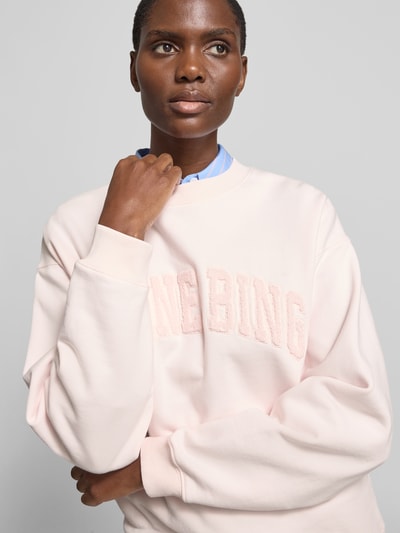 Frauenmodel trägt Regular Fit Sweatshirt mit Logo-Detail von Anine Bing in zartem Rosa, Reine Baumwolle, elastische Abschlüsse, Rundhalsausschnitt, Rückenlänge bei Größe S 65 cm, Nahaufnahme Oberkörper.