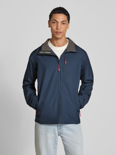Männermodel trägt Regular Fit Jacke mit Stehkragen Modell 'Crew' von Helly Hansen, dunkelblau mit Logo-Print und Reißverschlusstaschen, Ganzkörperansicht von vorne. Herren Jacke mit Napoleontasche, Eingrifftaschen mit Reißverschluss, Rückenlänge 73 cm, Schulterbreite 48 cm, Brustweite 56 cm, Ärmellänge 68 cm.