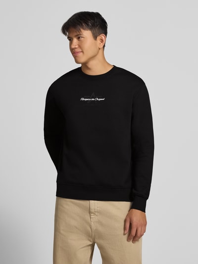 Männermodel trägt Regular Fit Sweatshirt aus Baumwoll-Mix mit Label-Detail von Alpha Industries, schwarz, elastische Abschlüsse, Ganzkörperansicht von vorne. Rückenlänge bei Größe M: 66 cm.