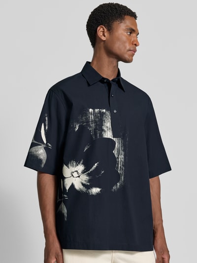 Männermodel trägt Regular Fit Poloshirt aus reiner Baumwolle von Armani Exchange mit floralem Design, Dunkelblau und Weiß, Nahaufnahme Oberkörper.