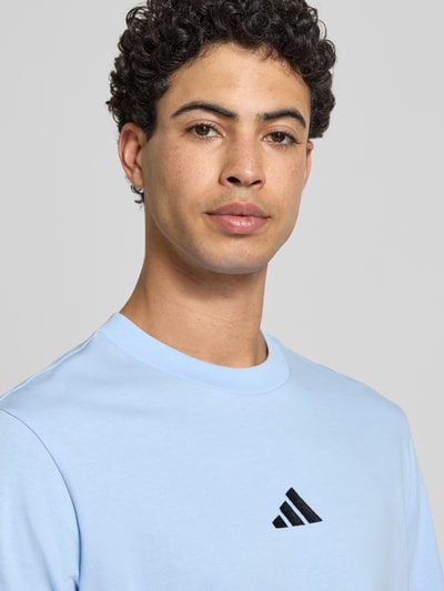 Männermodel trägt T-Shirt mit Label-Detail von adidas Sportswear in Hellblau aus reiner Baumwolle, Nahaufnahme Oberkörper.