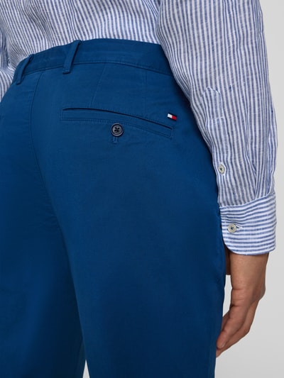 Männermodel trägt Regular Fit Chino aus Baumwoll-Mix Modell "Denton" von Tommy Hilfiger in Blau mit Logo-Patch und Gesäßtasche, Nahaufnahme Rückansicht.