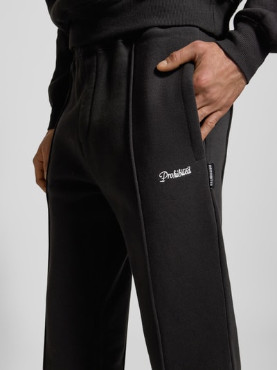 Männermodel trägt Sweatpants mit elastischem Bund von PROHIBITED aus schwarzem Baumwoll-Mix mit Label-Stitching und französischen Eingrifftaschen, lockerer Schnitt, Detailaufnahme Hüfte und Bein.