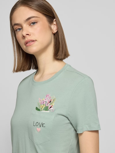 Frauenmodel trägt Regular Fit T-Shirt aus reiner Bio-Baumwolle Modell 'POLLY' von Only in Optik: Unifarben mit Statement-Print-Applikation und Motiv-Stitching, Rundhals-Ausschnitt, Kurzarm, Brusttasche, Materialverarbeitung: Jersey, Nahaufnahme Oberkörper.