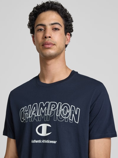 Männermodel trägt T-Shirt mit Label-Print und Rundhalsausschnitt von CHAMPION in Dunkelblau, Reine Baumwolle, Regular-Fit, Nahaufnahme Oberkörper.