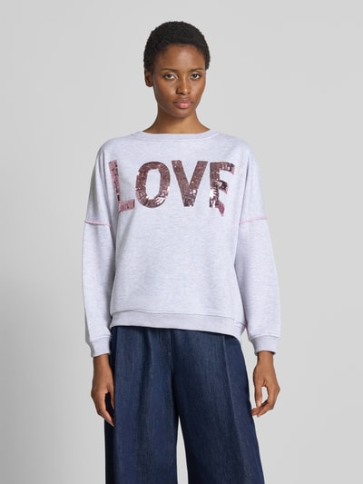 Vrouwenmodel draagt oversized sweatshirt uit puur katoen Model 'Love' van miss goodlife, lichtgrijs met Statementprint en pailletten, ronde hals, elastische boorden, vooraanzicht, close-up bovenlichaam.