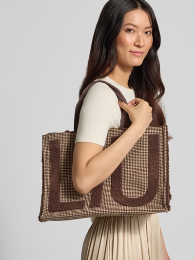 Kobiece model prezentuje Tote Bag z detalami z logo od Liu Jo White, beżowy i brązowy, Główna przegroda z zamkiem błyskawicznym, Odpinany pasek na ramię, krótkie uchwyty, przegródka wewnętrzna zapinana na zamek błyskawiczny, Szerokość w rozmiarze 1: 42 cm, Długość w rozmiarze 1: 30 cm, Głębokość w rozmiarze 1: 20 cm, długość paska na ramię w rozmiarze 1: 42 cm, wyraźna faktura tkaniny, prostokątny kształt, brązowy napis na powierzchni, jednolite tło, całkowity widok z przodu