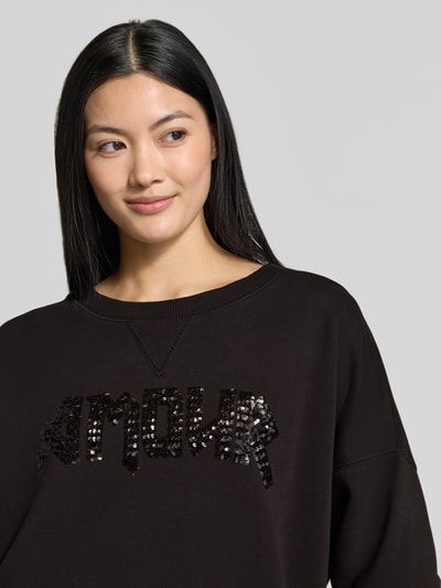 Frauenmodel trägt Relaxed Fit Sweatshirt aus reiner Baumwolle von miss goodlife mit Pailettenbesatz und Statement-Design, Nahaufnahme Oberkörper.