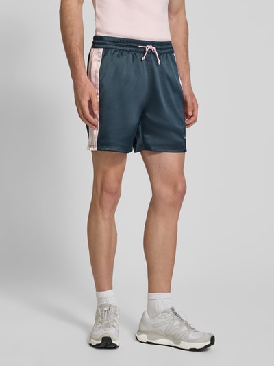 Männermodel trägt Shorts aus Satin mit Label-Stitching und elastischem Bund von BLKVIS in Dunkelblau mit rosa Details, Ganzkörperansicht von vorne. Herren Shorts, Regular-Fit, Tunnelzug, Bundweite 42 cm, Innenbeinlänge 14 cm, Satin-Optik.