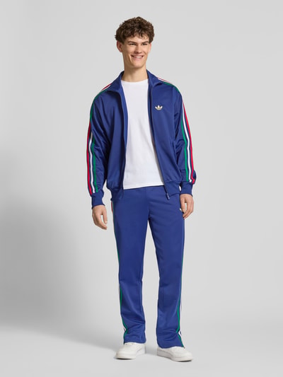 Mannenmodel draagt Regular Fit trainingsjack met meerkleurige contraststrepen model 'FIREBIRD TT' van adidas Originals, look: effen, regular fit pasvorm, ritssluiting, gestikt logo, details: meerkleurige contraststrepen, opstaande kraag, mouwboord en rompzoom: geribd, zij-ritszak, geheellichaamsfoto van voren.