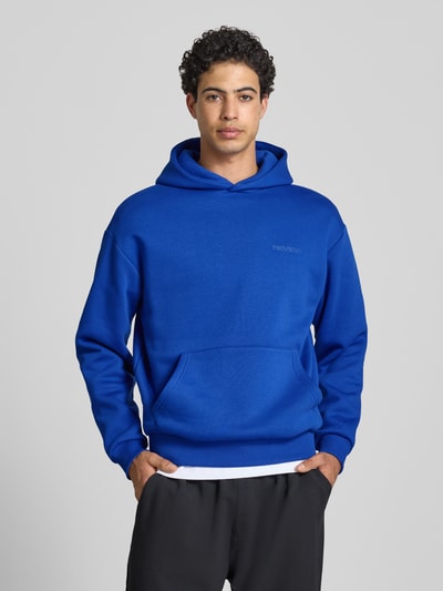 Männermodel trägt Hoodie mit Känguru-Tasche von REVIEW in Blau, lockere Passform, Kapuze, elastische Abschlüsse, Nahaufnahme Oberkörper.