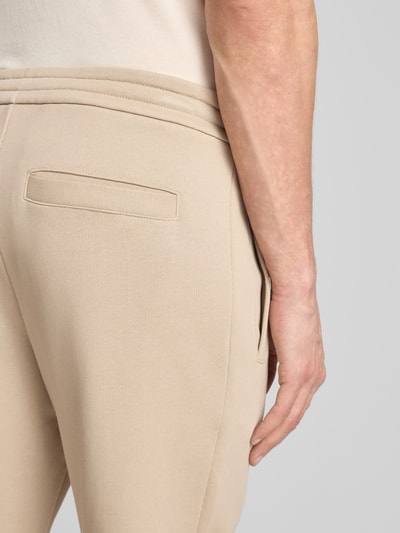 Männermodel trägt Regular Fit Sweatpants aus reiner Baumwolle von ARMANI EXCHANGE in Beige mit Gesäßtasche, Detailaufnahme Hüfte.