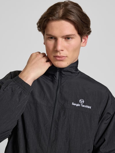 Männermodel trägt Regular Fit Jacke mit stójka Modell 'Nayla' von SERGIO TACCHINI, czarny kolor, zamek błyskawiczny, wpuszczane kieszenie, elastyczne wykończenia, długość tyłu w rozmiarze M 69 cm, długość rękawów 61 cm, krój regular fit, nahaufnahme górnej części ciała.