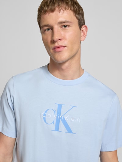 Männermodel trägt T-Shirt mit Label-Print und Rundhalsausschnitt von Calvin Klein Jeans in Hellblau, Reine Baumwolle, Regular-Fit, Nahaufnahme Oberkörper.