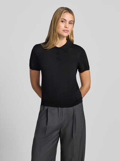Frauenmodel trägt schwarzes, tailliertes Poloshirt aus Viskose-Mix Modell 'LUXEN' von MANGO, gerippte Abschlüsse, Nahaufnahme Oberkörper.
