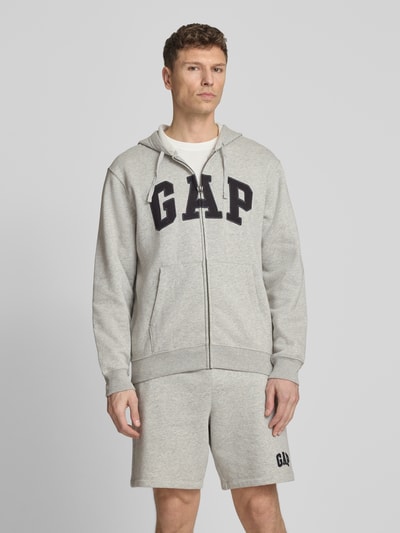 Männermodel trägt Sweatjacke mit Logo und Känguru-Tasche von GAP in Grau, Baumwoll-Mix, Regular-Fit, Ganzkörperansicht von vorne.