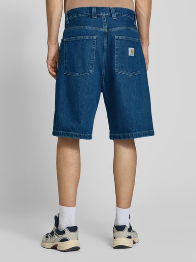 Männermodel trägt Jeansshorts mit Eingrifftaschen Modell 'Brandon' von Carhartt Work In Progress in Blau, lockerer Schnitt, Ganzkörperansicht Rückansicht. Reine Baumwolle, Relaxed Fit, Bundweite 44 cm, Innenbeinlänge 25 cm.
