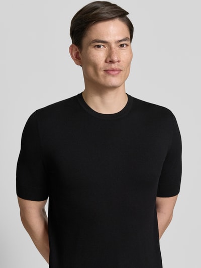 Männermodel trägt Slim Fit T-Shirt aus Strick von HUGO in Schwarz mit Rundhalsausschnitt und Label Stitching, Nahaufnahme Oberkörper.
