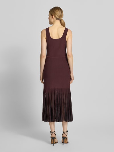 Modelka nosi Strickkleid aus Rippstrick od BOSS, bordowy kolor, krój slim fit, długość do kolan, bez rękawów, plisy z transparentnego materiału, widok całej sylwetki z tyłu.
