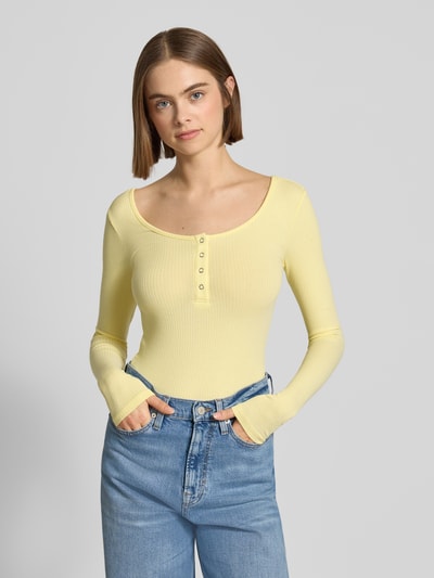 Kobiece model prezentuje Slim Fit Langarmshirt aus Baumwoll-Mix Modell 'KITTE' od Pieces, żółty, prążkowany, jednolity, długie rękawy, Henley, widok na cały tułów z przodu.