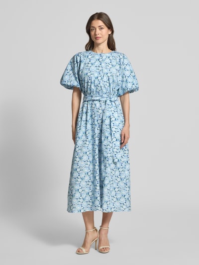 Modelka kobieca ma na sobie Midikleid mit Rundhalsausschnitt und Bindegürtel od Rich & Royal, niebieska bawełna, wzór allover, krój slim fit, długość tyłu w rozmiarze 36: 127 cm, szerokość w rozmiarze 36: 30 cm, długość rękawa w rozmiarze 36: 38 cm, widok całofigurowy z przodu.