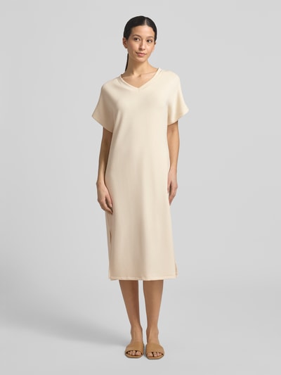 Modelka nosi T-Shirt-Kleid mit V-Ausschnitt od Soyaconcept, kolor beżowy, prosty krój, materiał z modalu, widok całej sylwetki z przodu.
