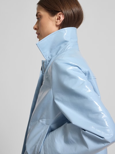 Frauenmodel trägt Jacke in glänzender Lackleder-Optik - curated by Vicky Heiler von SIC in Hellblau mit Umlegekragen und Eingrifftaschen, glatte Textur, Nahaufnahme Oberkörper, Kontext: Boxy Fit, Rückenlänge 50 cm, Schulterbreite 41 cm, Brustweite 52 cm, Ärmellänge 60 cm.