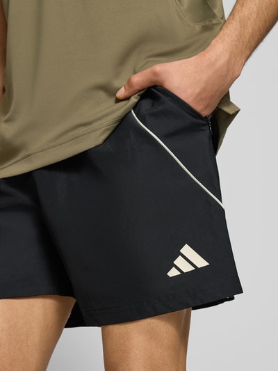 Männermodel trägt Regular Fit Sport-Shorts mit Kontraststreifen von adidas Sportswear, Optik: Unifarben, Logo-Print, Nahaufnahme Oberschenkel.