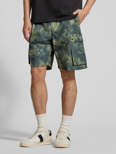 Männermodel trägt Shorts mit Cargotaschen Modell 'Ethan' von Wood Wood aus Baumwoll-Mix in Relaxed-Fit, Batikmuster, Ganzkörperansicht von vorne. Bundweite bei Größe M: 41 cm, Innenbeinlänge bei Größe M: 20 cm.