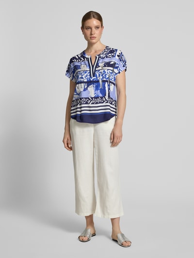 Frauenmodel trägt Blusenshirt aus Viskose mit Strasssteinbesatz von Betty Barclay, Motiv- und Statement-Print, Straight Fit, Tunikakragen, Kappärmel, reine Viskose, Farbverlauf in Blau-Weiß, Halbarm, strukturierte glatte Oberfläche, Rückenlänge bei Größe 36: 55 cm, Ärmellänge: 19 cm, Ganzkörperansicht von vorne.