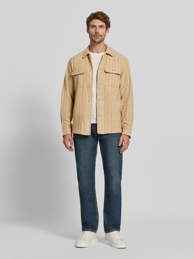 Männermodel trägt Relaxed Fit Hemdjacke mit Brusttaschen von Scotch & Soda, beige, grobe Textur, Allover-Look, Ganzkörperansicht von vorne.