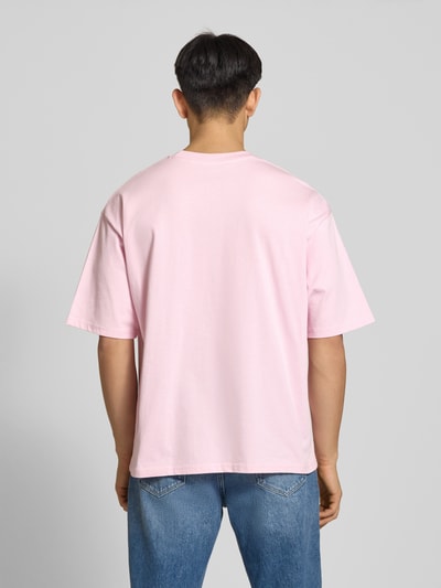 Männermodel trägt Oversized T-shirt mit logo en ronde hals van REVIEW, puur katoen, oversized, ruglengte maat M 68 cm, ganzkörperansicht rückansicht.