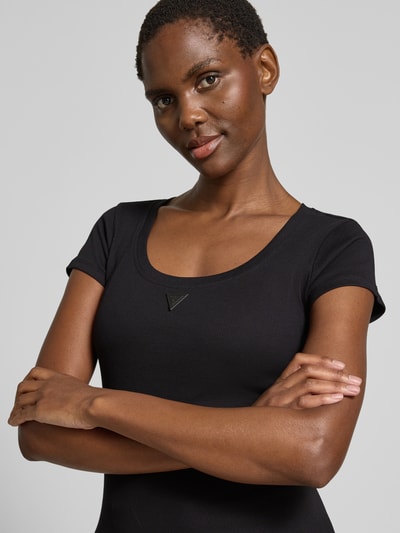 Frauenmodel trägt Slim Fit T-Shirt mit Logo-Applikation von Guess aus elastischem Baumwoll-Mix, Rundhalsausschnitt, Nahaufnahme Oberkörper.